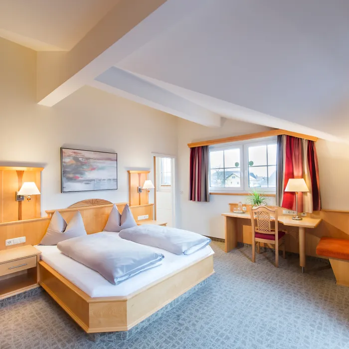 Helles Hotelzimmer mit Doppelbett, Schreibtisch und großem Fenster mit roten Vorhängen